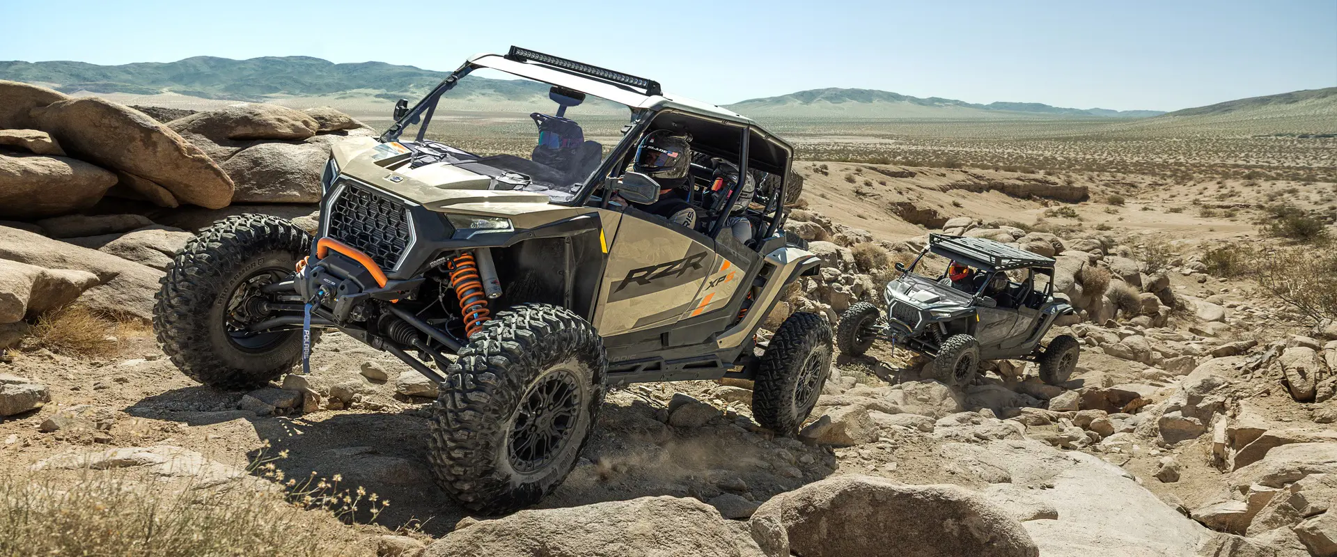 A 2026 Polaris RZR XP S 4 side-by-side climbing over rocky terrain in the desert with another RZR following behind.