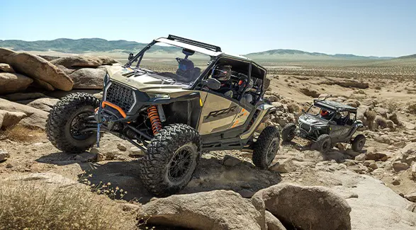 A 2026 Polaris RZR XP S 4 side-by-side climbing over rocky terrain in the desert with another RZR following behind.