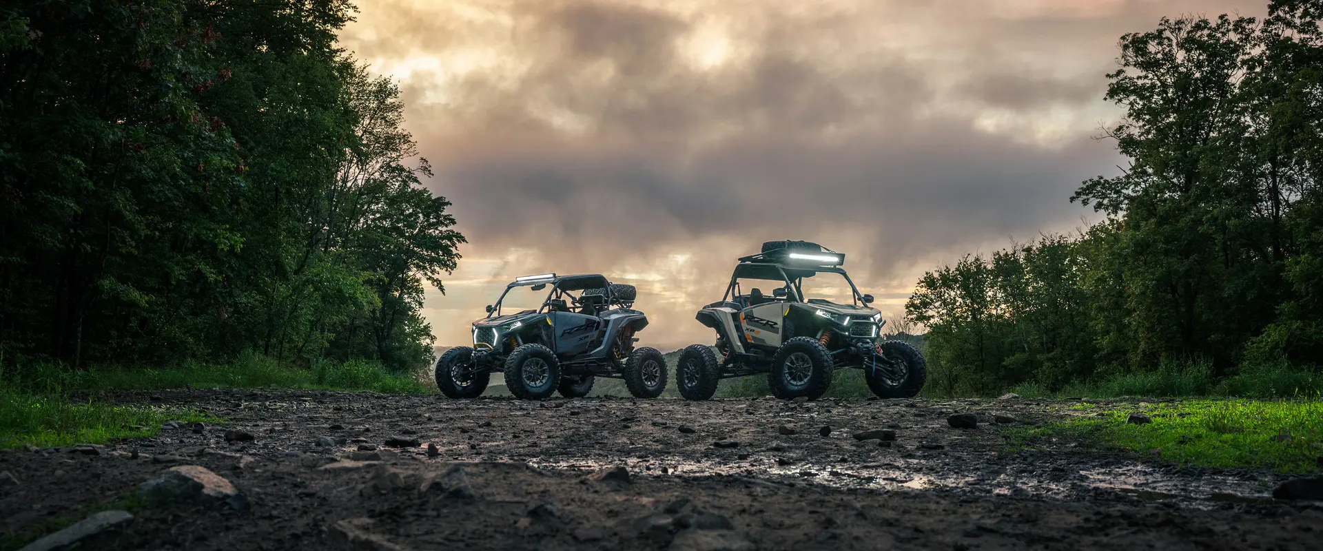 Two 2026 Polaris RZR XP S side-by-sides parked in an open muddy area with forest surrounding them.