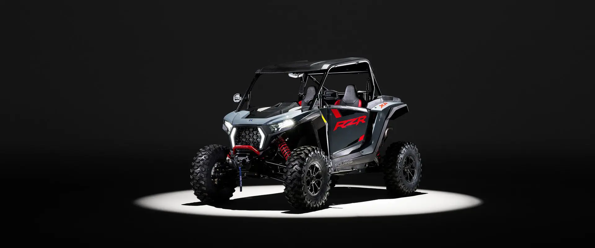 A 2026 Polaris RZR XP Ultimate SxS in the Stealth Gray colorway entrenched in light while parked in a dark garage.