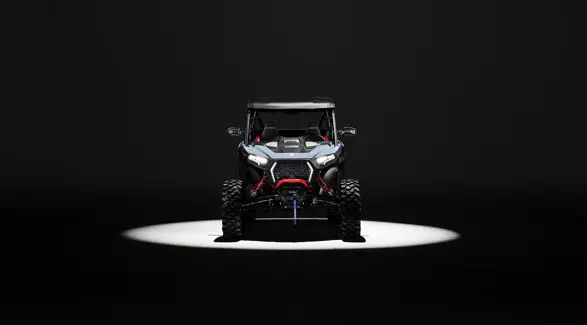 Front end view of a 2026 Polaris RZR XP Ultimate SxS in the Stealth Gray colorway entrenched in light while parked in a dark garage.