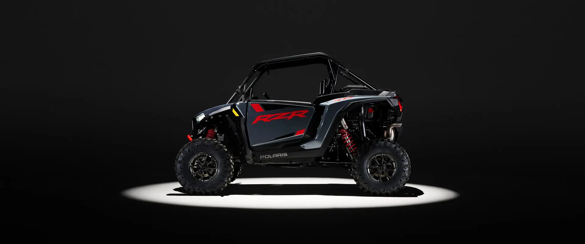 Side profile of a 2026 Polaris RZR XP Ultimate SxS in the Stealth Gray colorway entrenched in light while parked in a dark garage.