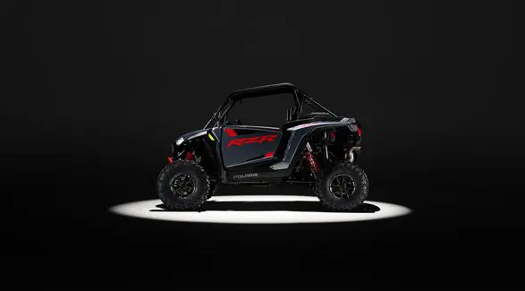 Side profile of a 2026 Polaris RZR XP Ultimate SxS in the Stealth Gray colorway entrenched in light while parked in a dark garage.