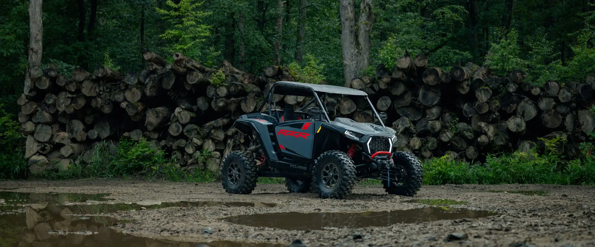 A 2026 Polaris RZR XP Ultimate SxS in the Stealth Gray colorway parked near a logged out forest.
