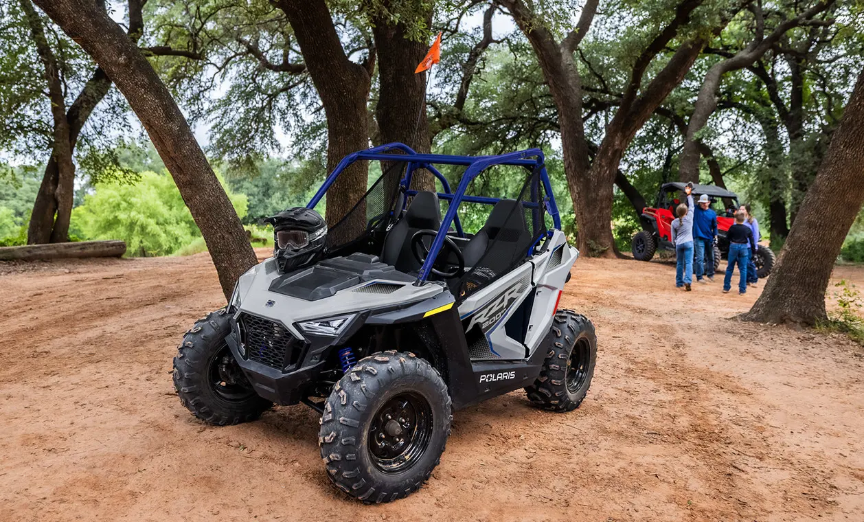 A 2027 Polaris RZR 200 EFI youth side-by-side in the Storm Gray colorway parked with a helmet on the hood.