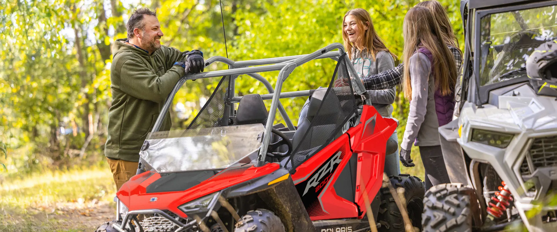 3 girls and a man chatting around a 2027 Polaris RZR 200 EFI youth side-by-side.