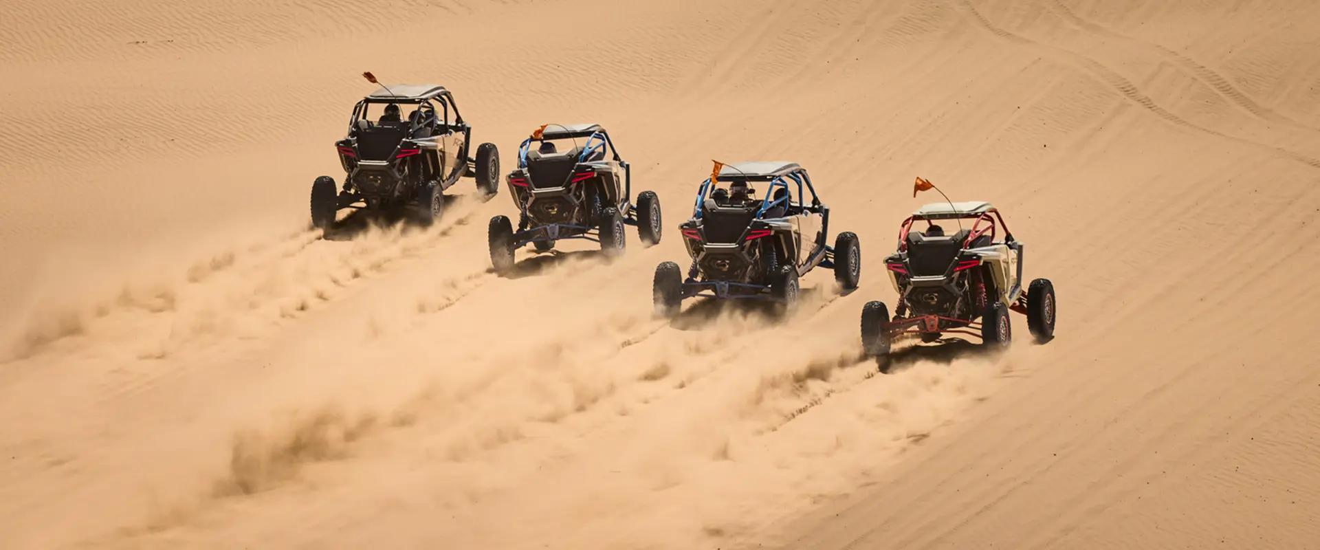 Four 2027 Polaris RZR Pro R Boost side-by-sides driving through the dunes.