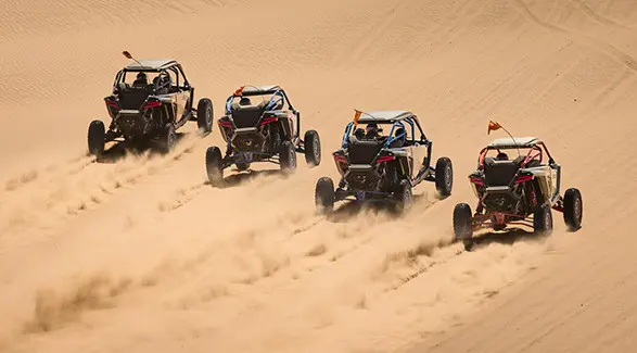 Four 2027 Polaris RZR Pro R Boost side-by-sides driving through the dunes.