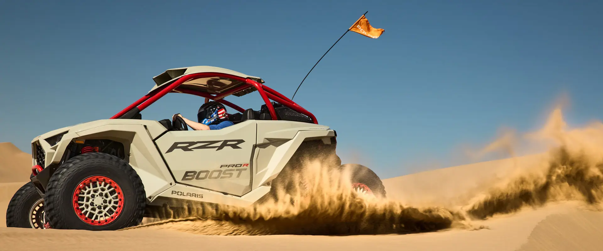 Side profile of a 2027 Polaris RZR Pro R Boost Ultimate side-by-side throwing sand in the desert.