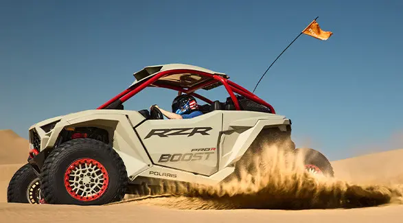 Side profile of a 2027 Polaris RZR Pro R Boost Ultimate side-by-side throwing sand in the desert.