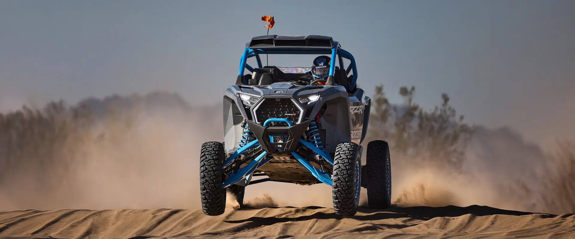 A driver in a 2027 Polaris RZR Pro R Boost Ultimate side-by-side cruising through the desert.