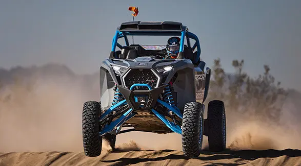 A driver in a 2027 Polaris RZR Pro R Boost Ultimate side-by-side cruising through the desert.