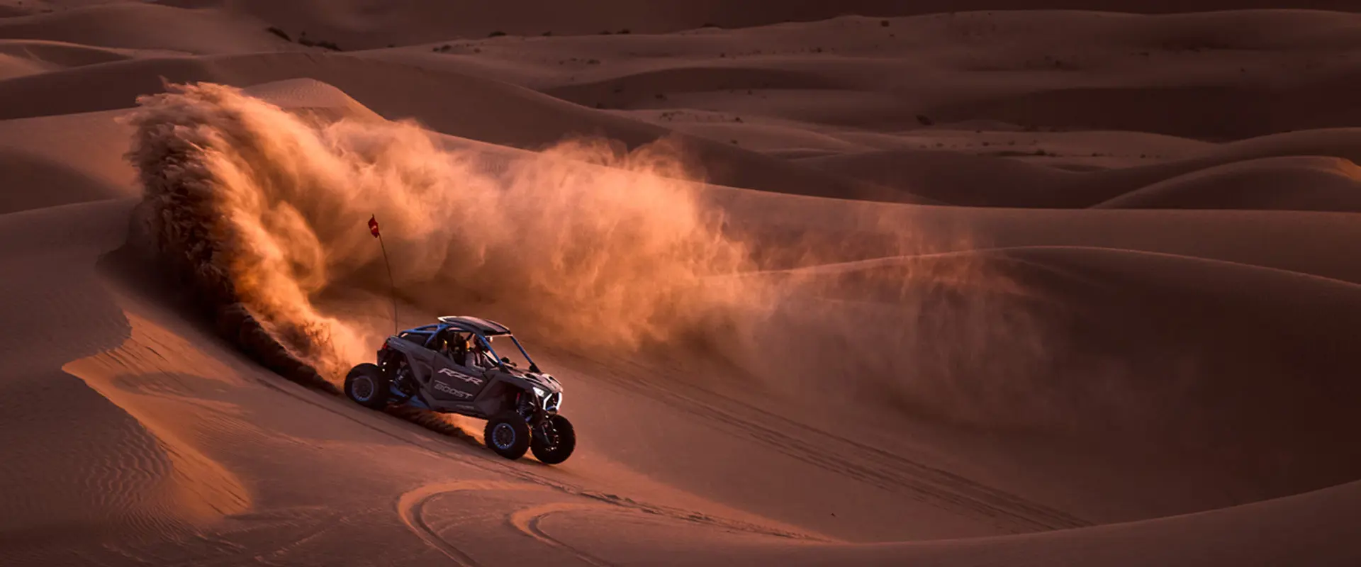 Side profile of a 2027 Polaris RZR Pro R Boost Ultimate side-by-side descending a dune in the desert.