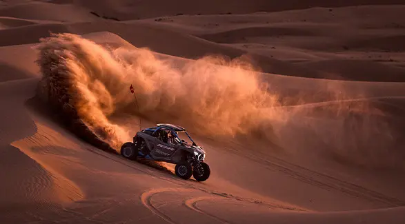 Side profile of a 2027 Polaris RZR Pro R Boost Ultimate side-by-side descending a dune in the desert.