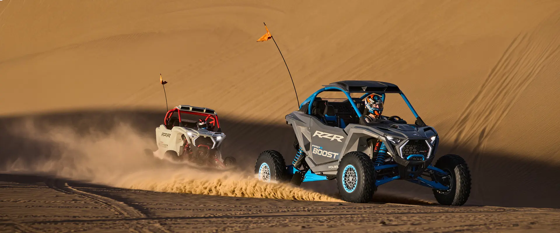 Two 2027 Polaris RZR Pro R Boost Ultimate side-by-sides climbing a dune in the desert.