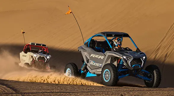 Two 2027 Polaris RZR Pro R Boost Ultimate side-by-sides climbing a dune in the desert.