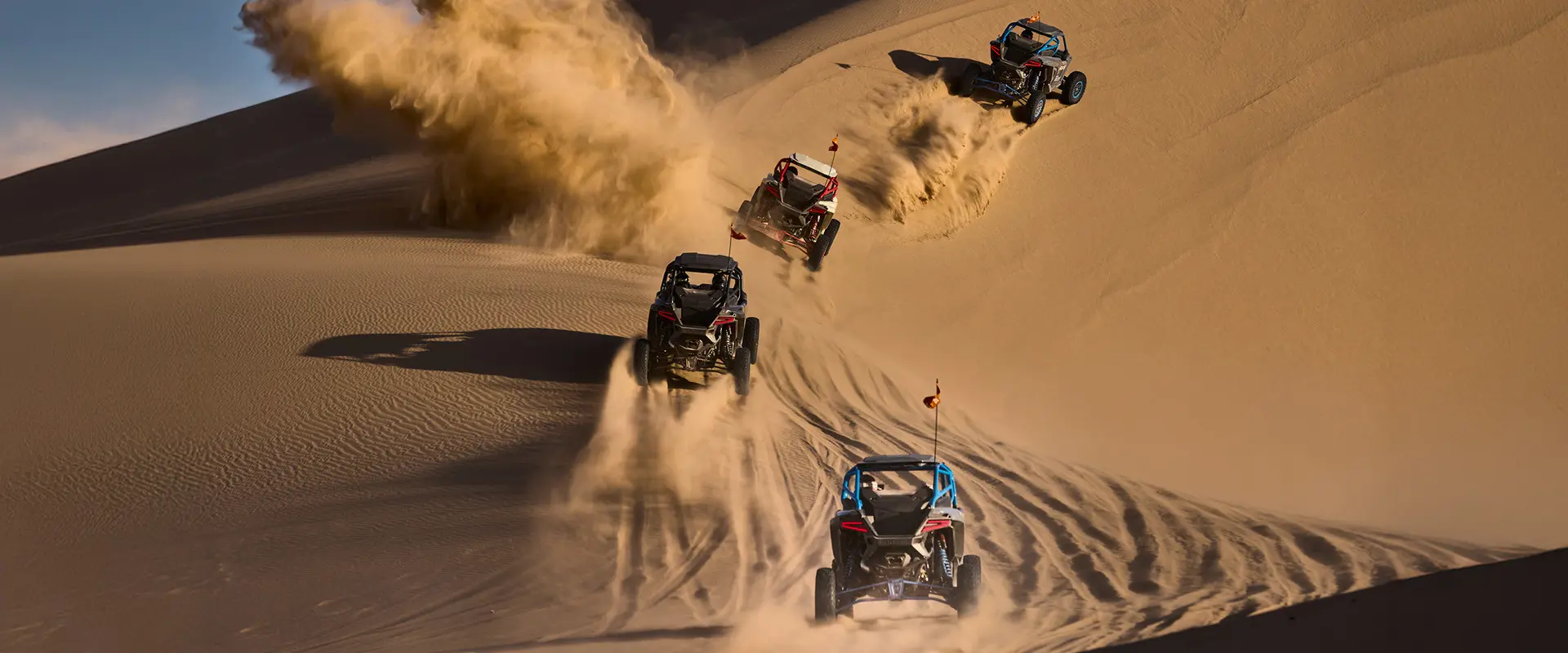 Four 2027 Polaris RZR Pro R Boost side-by-side climbing dunes in the desert.