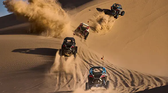 Four 2027 Polaris RZR Pro R Boost side-by-side climbing dunes in the desert.