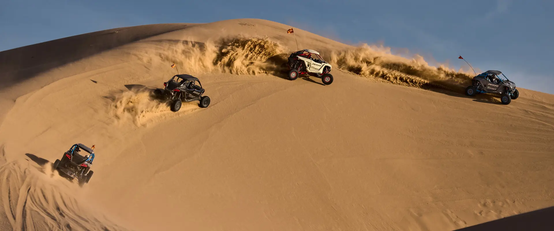 Four 2027 Polaris RZR Pro R Boost side-by-sides making a turn on a dune in the desert.
