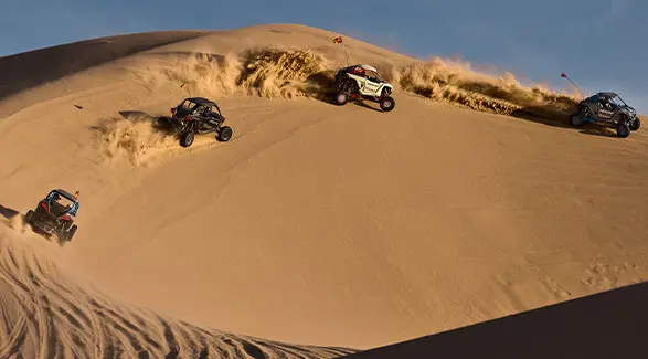 Four 2027 Polaris RZR Pro R Boost side-by-sides making a turn on a dune in the desert.
