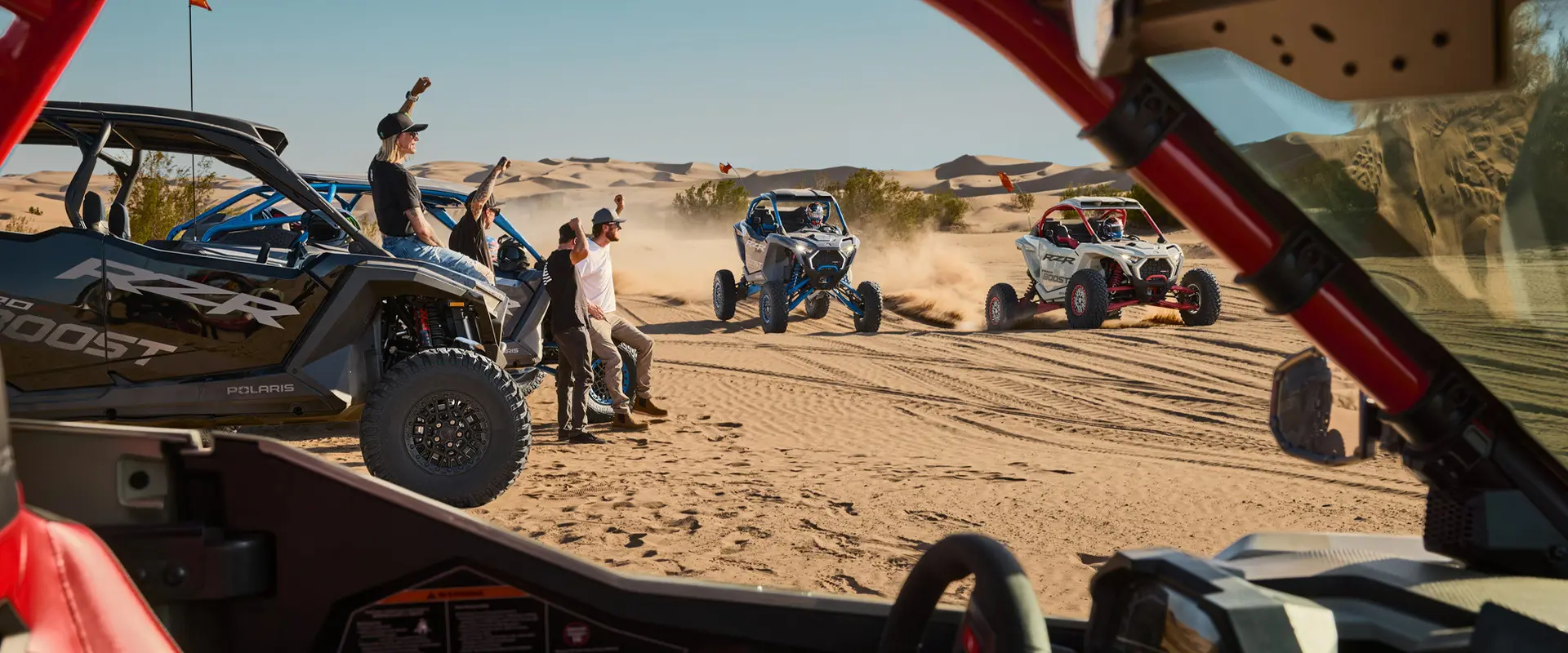 4 people cheering on two 2027 Polaris RZR Pro R Boost Ultimate side-by-sides in the desert.