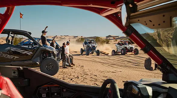 4 people cheering on two 2027 Polaris RZR Pro R Boost Ultimate side-by-sides in the desert.