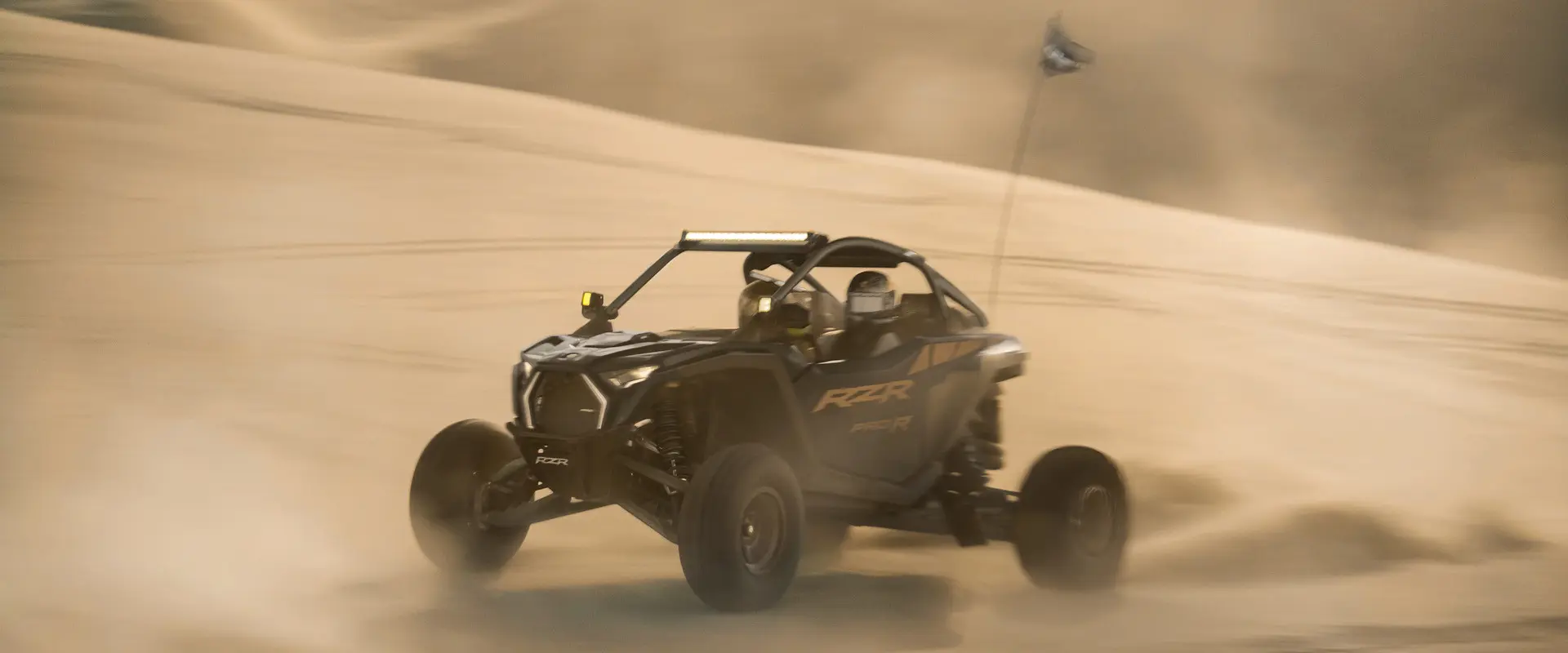 Side profile of 2 riders in a 2027 Polaris RZR Pro R side-by-side in the desert.