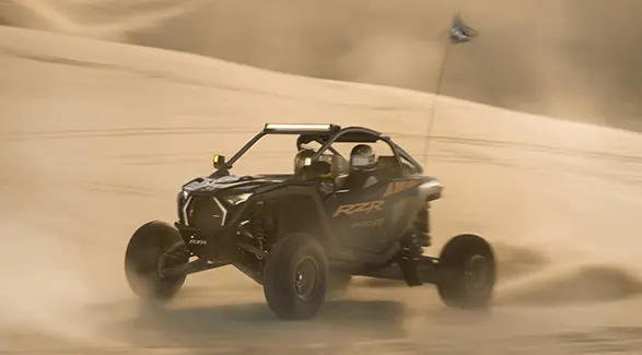 Side profile of 2 riders in a 2027 Polaris RZR Pro R side-by-side in the desert.