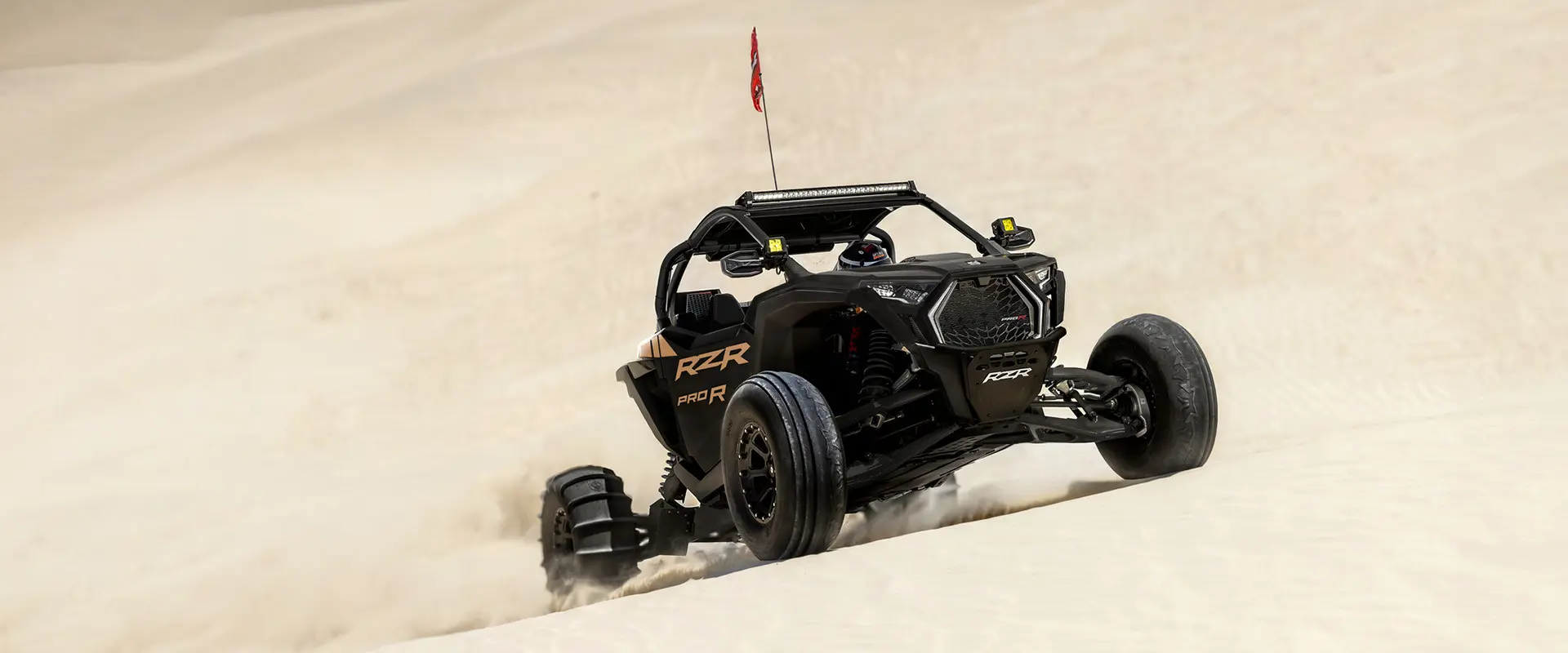 A rider in a 2027 Polaris RZR Pro R side-by-side climbing up a dune.