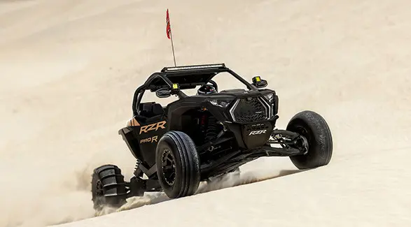 A rider in a 2027 Polaris RZR Pro R side-by-side climbing up a dune.
