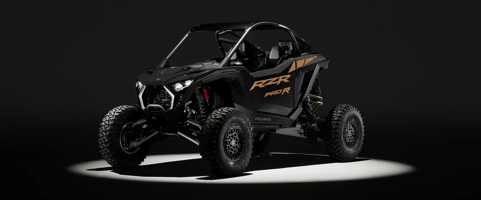 Front angle of a 2027 Polaris RZR Pro R side-by-side entrenched in light in a dark room.