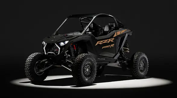 Front angle of a 2027 Polaris RZR Pro R side-by-side entrenched in light in a dark room.
