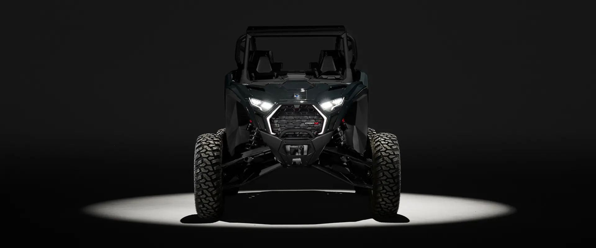 Front view of a 2027 Polaris RZR Pro R side-by-side entrenched in light in a dark room.