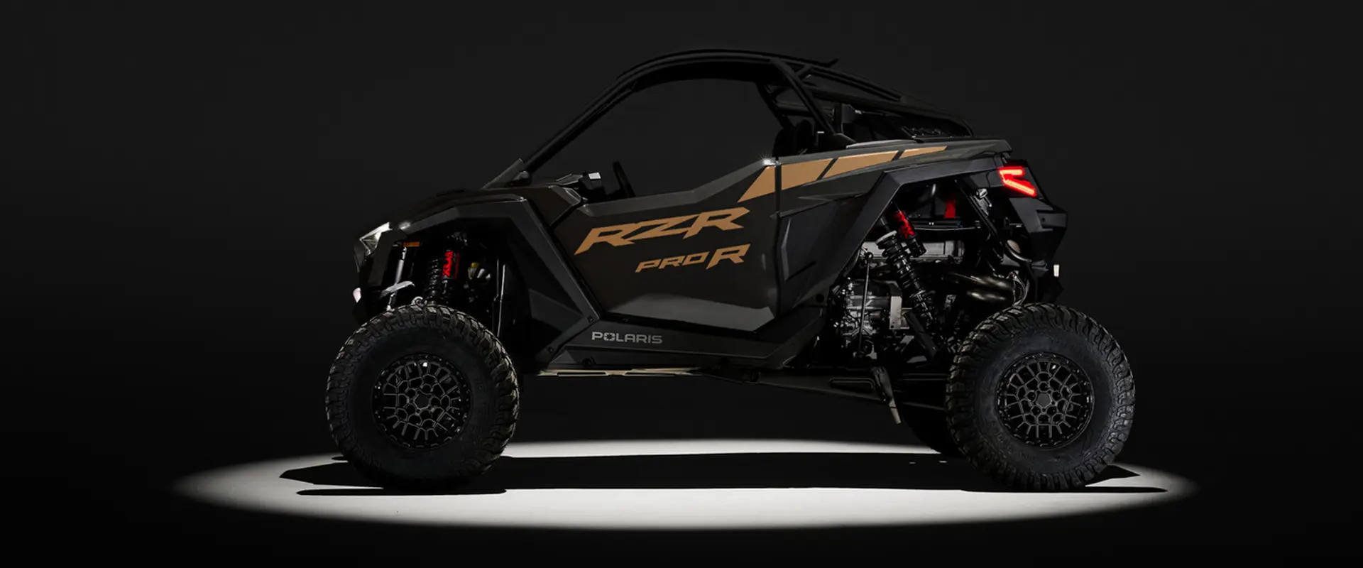 Side profile of a 2027 Polaris RZR Pro R side-by-side entrenched in light in a dark room.