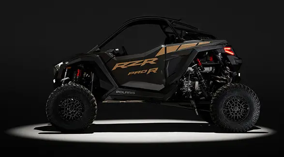 Side profile of a 2027 Polaris RZR Pro R side-by-side entrenched in light in a dark room.