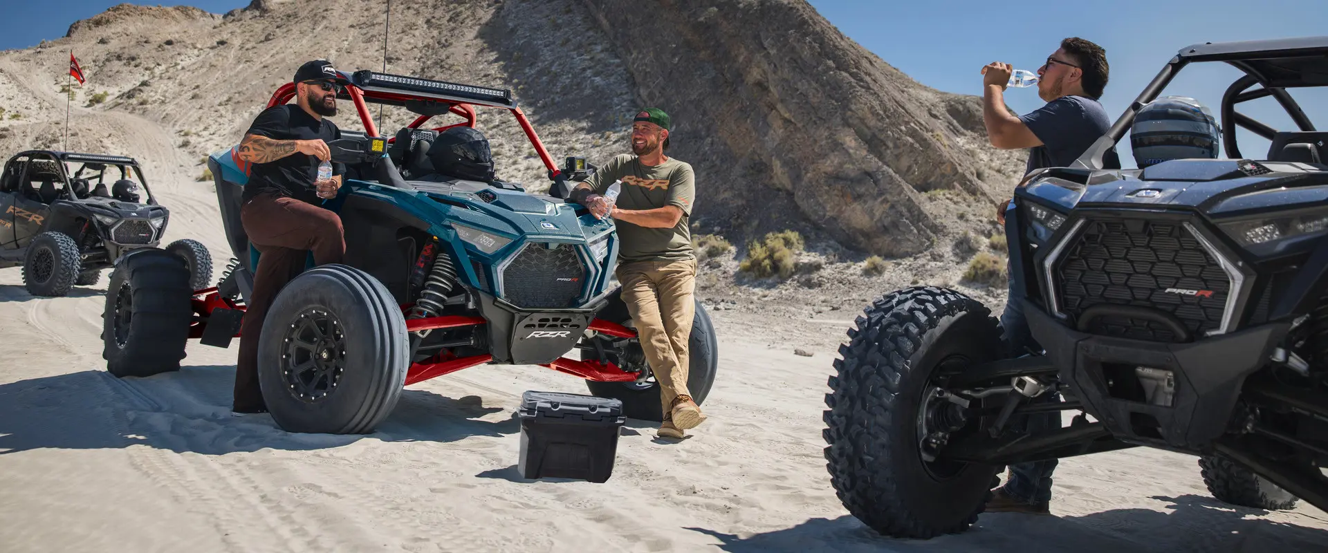 3 people relaxing after a ride in their 2027 Polaris RZR Pro R side-by-sides.