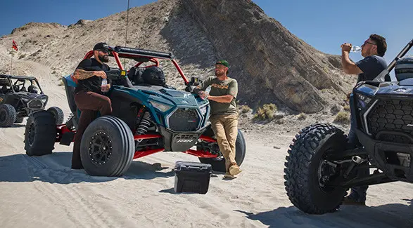 3 people relaxing after a ride in their 2027 Polaris RZR Pro R side-by-sides.