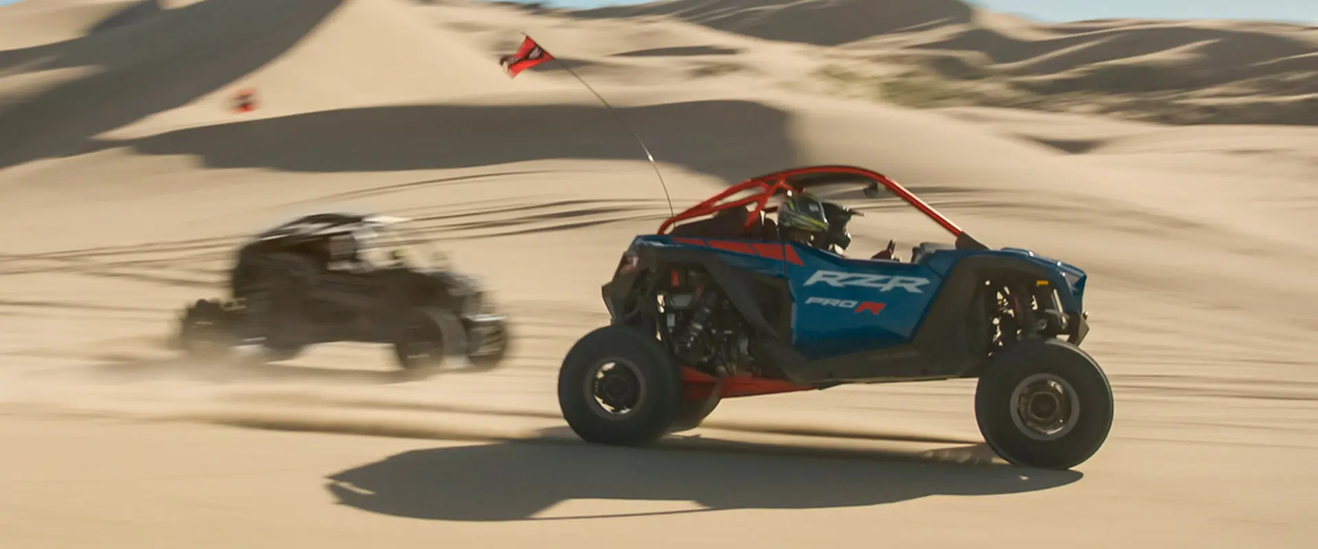 Side profile of two 2027 Polaris RZR Pro R side-by-side cruising through the desert.
