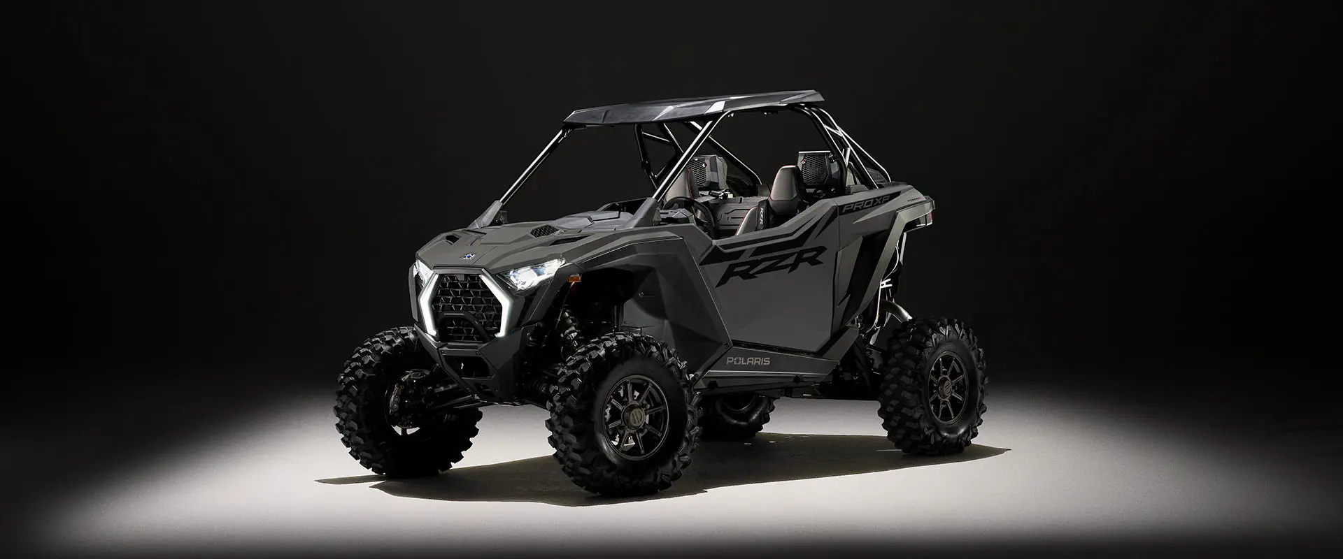 Side profile of a 2027 Polaris RZR Pro XP side-by-side entrenched in light in a dark room.