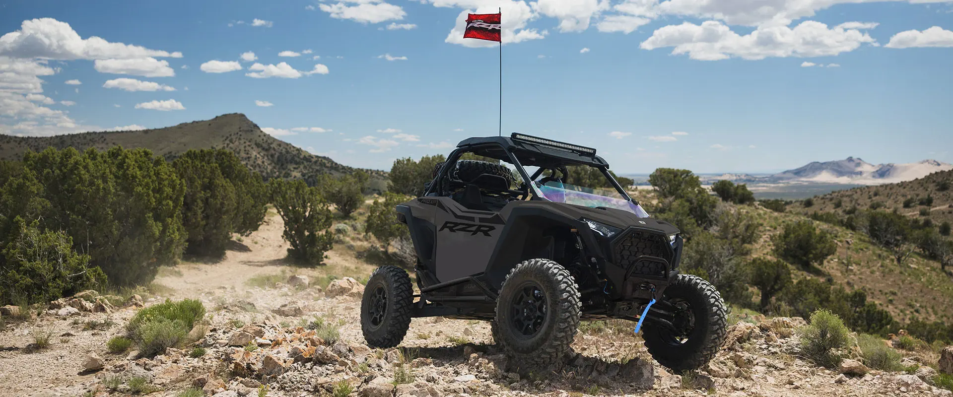 A 2027 Polaris RZR Pro XP side-by-side with it's flag up parked on a sunny day with blue skies.