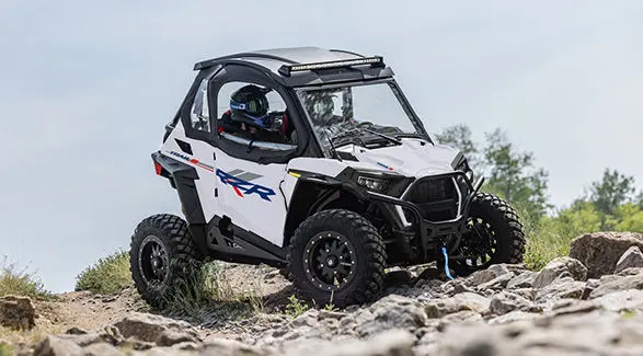 2 riders in a 2027 Polaris RZR Trail S side-by-side crawling over rocky terrain.