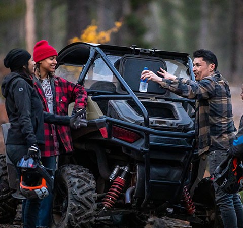 4 people around the cargo area of their 2027 Polaris RZR Trail SxS.