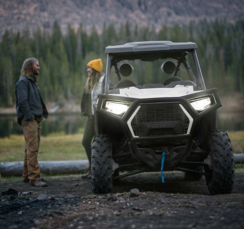 Front end view of the illuminated headlights of a 2027 Polaris RZR Trail SxS.