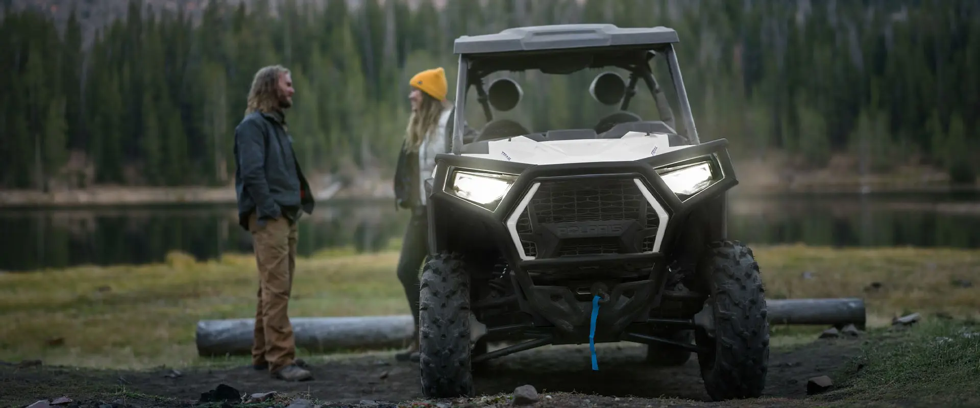 2 people standing behind a parked 2027 Polaris RZR Trail side-by-side.