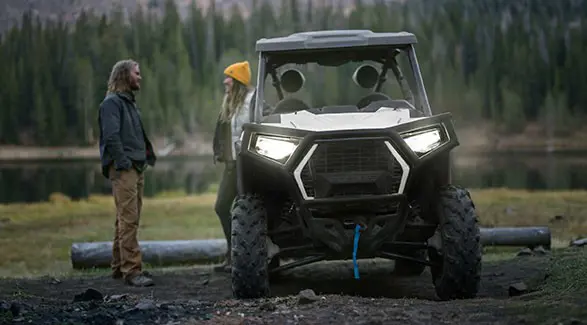 2 people standing behind a parked 2027 Polaris RZR Trail side-by-side.