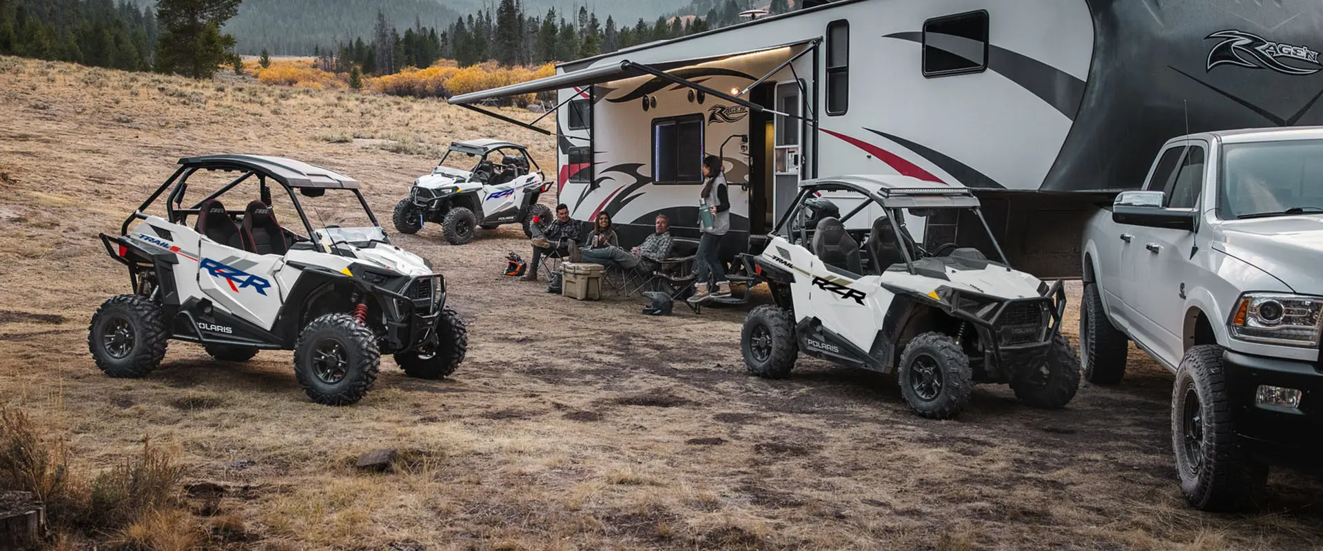 People sitting by their camper with three 2027 Polaris RZR Trail side-by-sides parked nearby.