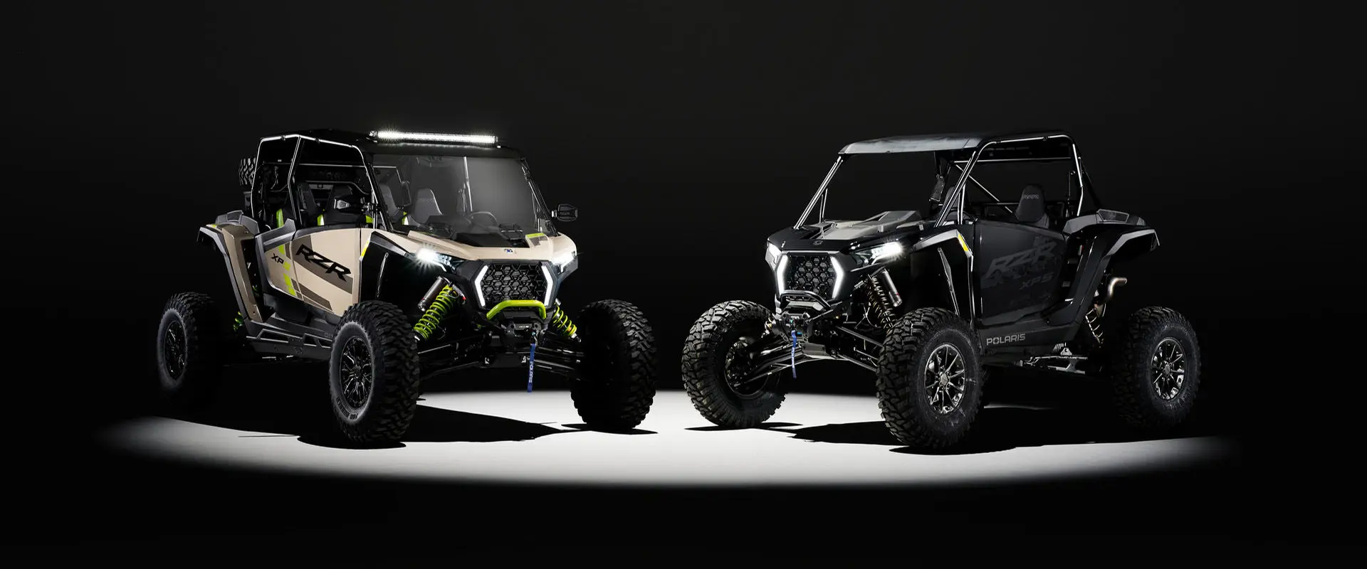 A 2027 Polaris RZR XP S 4 and a 2027 Polaris RZR XP S side-by-side entrenched in light in a dark room.