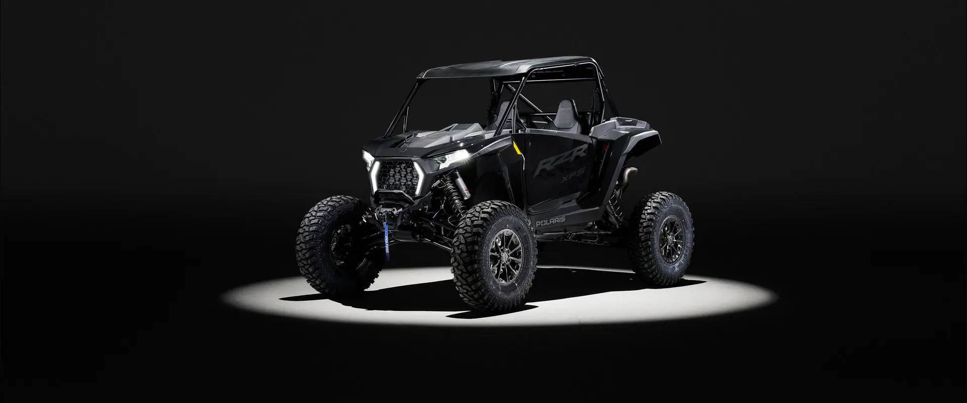 Front angle of a 2027 Polaris RZR XP S side-by-side entrenched in light in a dark room.