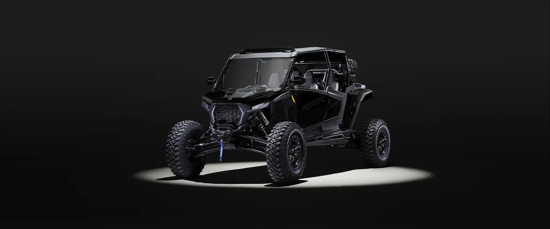 An Onyx Black 2027 Polaris RZR XP S 4 Ultimate side-by-side entrenched in light in a dark room.