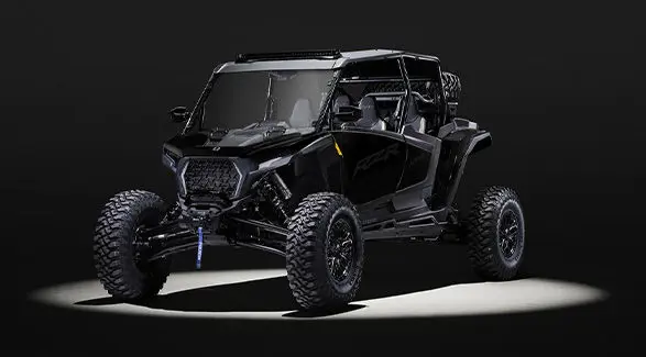 An Onyx Black 2027 Polaris RZR XP S 4 Ultimate side-by-side entrenched in light in a dark room.